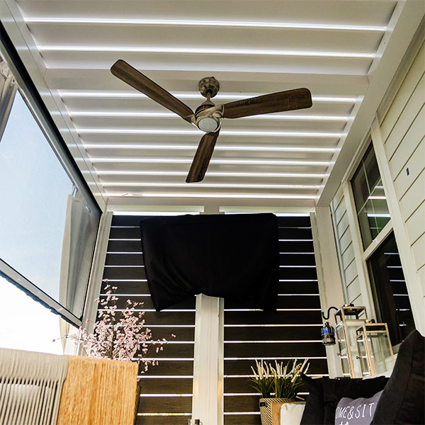 Cozy outdoor room covered with a motorzied louevred pergola in Chesapeake, VA. Model R-Blade electric roof in white accessorized with fan, tv, privacy screens and bug screens - Azenco